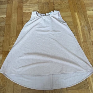 Ljusrosa ärmlös klänning från LMTD - Supersöt ljusrosa klänning från LMTD med rund hals och ärmlös design. Klänningen har en lätt A-linjeformad siluett och är något längre baktill för en cool look. Materialet är mjukt och har en diskret struktur som ger extra känsla.