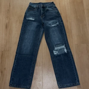 Mörkblå raka jeans med slitningar - Snygga mörkblå jeans med raka ben och slitna detaljer på låret och knät. Jeansen har klassisk femficksdesign, hög midja och är tillverkade i robust denim. Perfekta för en avslappnad och trendig look.