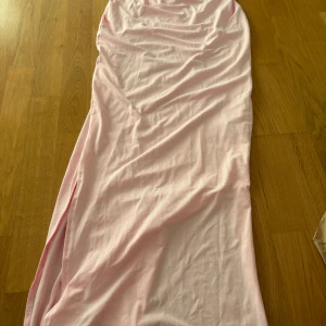 Ljusrosa långklänning i bomull - En enkel och stilren ljusrosa långklänning i mjuk bomull. Klänningen har omlott-detalj upptill och en slits på sidan för en snygg touch. Perfekt för varma dagar och har en skön, loose passform.