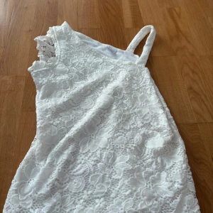 Vit spetsklänning/tröja från Lindex - Superfin vit klänning/tröja från Lindex med ett vackert blommigt spetsmönster. Klänningen har en axelbandslös sida och en axel med spetsdetalj, vilket ger en unik och trendig look. Perfekt för sommarens alla tillfällen!