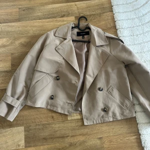 Beige kort trenchcoat - kort trenchcoat från vero moda, den är aldrig använd så är i nyskick!🤍