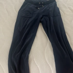 Mörkblå mjukisbyxor Juicy Couture S - Mörkblå mjukisbyxor från Juicy Couture i mjuk velour med snörning i midjan och två stora fickor fram. Broderad JC-logga på benet och silver detaljer på snöret. Perfekta för en chill och avslappnad look.