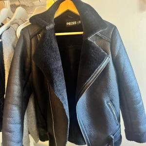 Svart teddyjacka från Pieces, stl S - Säljer en svart teddyjacka från Pieces i storlek S. Jackan har en bred krage, sned dragkedja och mjukt foder. Ytan är matt och lätt strukturerad, med detaljer i skinnimitation och dragkedjor vid fickorna. Perfekt för kalla dagar och riktigt snygg till jeans..Pris kan diskuteras 