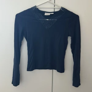 Mörkblå långärmad tröja med spets - Mörkblå långärmad topp från Gina Tricot med snygg v-ringning dekorerad med spetsdetaljer. Toppens material är mjukt och stretchigt, perfekt för en stilren look. Passformen är normal och toppen har en enkel, clean design med spetsen som extra detalj.