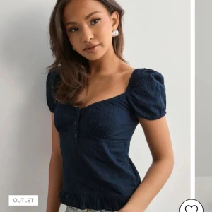 Mörkblå blus med puffärmar - Supersöt mörkblå blus med puffiga korta ärmar, knappar framtill. Toppen har en feminin v-ringning och volangkant nertill. Perfekt att styla med jeans. Bara anständ 2-3 gånger. Kan diskutera priss.