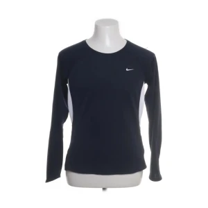 Nike Dri-Fit långärmad träningströja - Nike Dri-Fit långärmad träningströja i mörkblått med vita paneler på sidorna och liten vit Swoosh-logga på bröstet. Tillverkad i funktionsmaterial som andas och transporterar bort fukt. Perfekt för träning eller sportiga dagar.