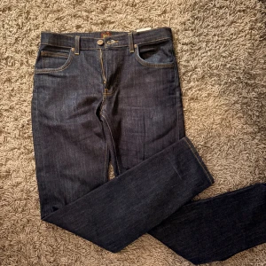 Mörkblå Lee Daren jeans W30 L32 - Snygga mörkblå Lee Daren jeans med klassisk femficksdesign och gul kontrastsöm. Modellen har rak passform och dragkedjegylf. Tillverkade i slitstarkt bomullsjeansmaterial, perfekta för en clean och stilren look.