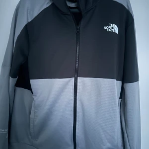 Grå och svart tröja från The North Face - Hej, säljer denna stilrena och fina trackjacket från The North Face. Jag har tyvärr bara tröjan och inget mer, men skulle säga att det är bara den som behövs ! Riktigt skön, lite stor i storleken men annars sitter den ganska bra, lite mer loose! Priset kan diskuteras!