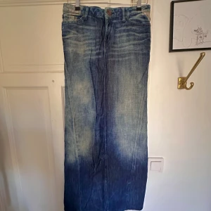 Lång jeanskjol från Replay - Säljer en lång klockformad jeanskjol från Replay i klassisk blå denim med slitna detaljer och fickor både fram och bak. Kjolen har en klockformad passform och stängs med knapp och dragkedja. Jag önskade jag kunde visa denna på för passformen är otrolig men den är tyvärr alldeles för liten för mig.. Kjolen är 99 cm lång och midemåttet mätt rakt över är 38 cm.