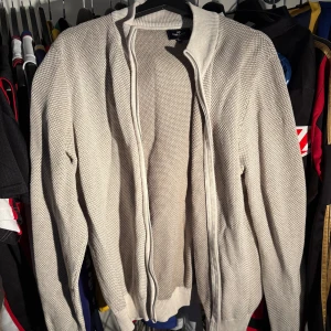 Beige stickad kofta med dragkedja - Snygg beige stickad kofta med dragkedja framtill och ribbade muddar. Perfekt för lager-på-lager och har en clean, klassisk look med diskret struktur i materialet. Passar dig som gillar stilrena och bekväma plagg.