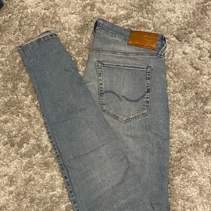 Ljusblå jeans från Jack and Jones - Säljer ett par jeans med klassisk femficksdesign och läderpatch bak i midjan. Jeansen har en smal passform och är tillverkade i mjukt denimtyg. Perfekta för dig som gillar en stilren och enkel look.
