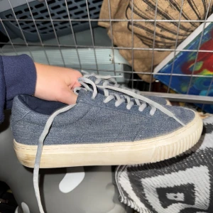 Grå denim-sneakers med vit sula - Snygga sneakers i blå denim-look med blå snörning och vit, platt gummisula. Skorna har en klassisk rund tå och enkel design som passar till det mesta. Perfekta för dig som gillar en stilren och avslappnad vibe.