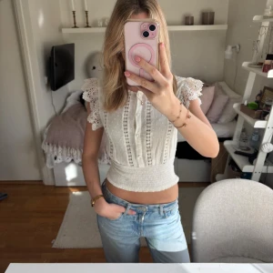 Vit blus med spetsärmar från pimkie, köpt från zalando  - Supersöt vit blus från pimkie/zalando med broderade spetsärmar och knappar framtill. Toppen har smockad midja, diskreta prickar i tyget och fina spetsdetaljer längs bröstet. Perfekt till jeans för en romantisk look.
