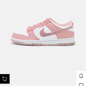 Nike Dunk Low rosa och vita sneakers - Nike Dunk Low sneakers i en snygg kombination av ljusrosa och vitt. Skorna har klassisk snörning, vit sula och rosa detaljer på swoosh och häl. Perfekta för dig som vill sticka ut med en fräsch och trendig look. Tillverkade i syntet och skinn.