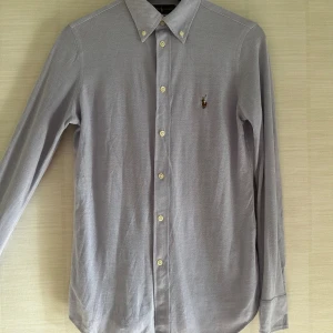 Ljusgrå skjorta från Ralph Lauren - Säljer en stilren ljusgrå skjorta från Ralph Lauren i klassisk oxfordmodell. Skjortan har button-down krage, broderad logga på bröstet och är tillverkad i bomull. Perfekt för dig som gillar en clean och tidlös look.