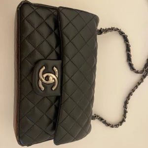 Svart quiltad axelväska - Säljer en svart axelväska i quiltat skinn med silverfärgad kedja och klassisk CC-logga framtill. Insidan har röd detalj med broderad logga och dragkedja. Väskan har lite slitage, se på bilderna annars superfin. Be om fler bilder