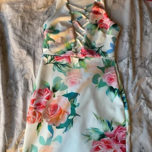 Blommig kortklänning med snörning - Superfin kortklänning i vit bas med stora blommiga mönster i rosa, grönt och persikotoner. Klänningen har en snygg snörningsdetalj framtill och är ärmlös med halterneck. Materialet känns mjukt och stretchigt, perfekt för sommarens alla tillfällen.+frakt 50❤️