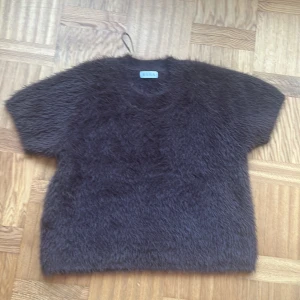 Mörkbrun fluffig topp från Wera - Säljer en mörkbrun, kortärmad och superfluffig topp, Grace från Wera. Den har en loose passform och är tillverkad i ett pälsliknande syntetmaterial som ger en unik och mysig look. Perfekt för dig som vill sticka ut med en cool textur och enkel design.