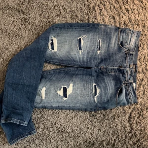 Blå ripped jeans Andy World WATERS - Säljer ett par blå jeans från Andy World, modell WATERS Carrot Stretch. Jeansen har flera slitningar och hål framtill för en riktigt edgy look. Klassisk femficksmodell med normal passform och dragkedja. Perfekta för dig som gillar streetstyle.