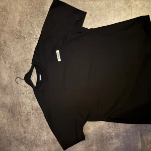 Svart t-shirt från Jacquemus - Svart t-shirt från Jacquemus i 100% bomull. Klassisk modell med kort ärm och rund halsringning. Diskret Jacquemus-logga framtill på bröstet. Perfekt för en clean och stilren look.