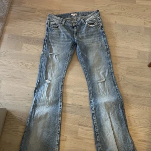 Ljusblå jeans med slitning - Säljer ett par ljusblå jeans med klassisk femficksdesign och en snygg slitning på ena benet, använt en gång men nu har dom blivit för stora 