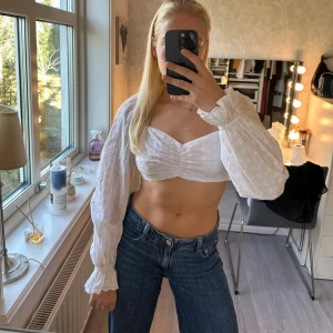 Vit broderad croppad blus med snörning - Superfin vit croppad blus med broderade blommor, långa ärmar och smock vid ärmslut. Toppen har u-ringning, rynk framtill och öppen rygg med snörning som knyts i ryggen. Perfekt för en trendig och söt look. Använd några gånger vid finare tillfällen men fortfarande i väldigt bra skick❣️