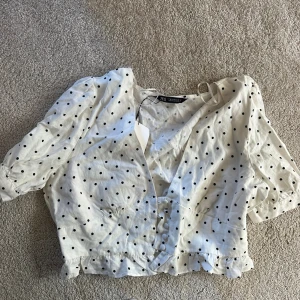 Prickig blus från Zara  - Supersöt vit blus från Zara med svarta prickar, v-ringning och knappar framtill. Blusen har korta puffärmar. Helt ny, aldrig använt. Lappen kvar. 