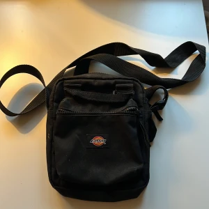 Dickies väska  - Liten axelremsväska från Dickies. Använd men inte trasig. Två fack med dragkedja och små fickor på insidan. Justerbart axelband! 