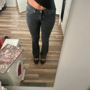Mörkgrå bootcut jeans - Säljer ett par mörkgrå jeans med bootcut passform och klassisk femficksdesign. Jeansen har normal midja och är tillverkade i ett mjukt denimtyg som sitter snyggt på benen. Perfekta för dig som gillar en enkel och stilren look.