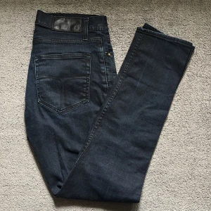 Mörkblå jeans Pistolero Skeletor 30/32 - Snygga mörkblå jeans från Pistolero, modell Skeletor. Klassisk femficksdesign med raka ben och diskreta sömmar. Jeansen har en svart läderpatch i midjan och är tillverkade i ett slitstarkt denimtyg. Perfekt för dig som gillar stilrena och tidlösa jeans.