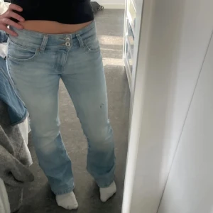 low waist jeans - Säljer ett par ljusblå jeans med bootcut-modell och låg midja. Storlek 34 och byxan har även ett litet hål vid sidan men tycker det ger en snygg detalj på byxorna