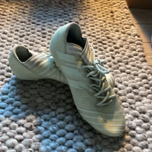 Adidas Nemeziz ljus grön fotbollsskor - Säljer ett par Adidas Nemeziz fotbollsskor i ljus grön färg med klassiska tre ränder på sidan och snörning framtill. Skorna har mönstrad ovandel och dobbar för spel på gräs. Perfekta för dig som vill sticka ut på planen.storlek 42 bra skick. Hör av dig om du har frågor eller funderingar!