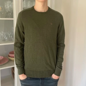 Grön merinoullströja från Morris - M - Jag säljer den här riktigt snygga merinoullströjan från Morris. Den är använd men fortfarande i jättebra skick utan skador. Storleken är M men den passar även S. Nypris ligger på 1599kr och jag säljer den här för 399kr. Tveka inte att höra av er!                                                                                               Måtten: Längd=66cm. Bredd=42cm.