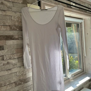 Vit långärmad klänning från 157 - En enkel och stilren vit långärmad klänning från 157 med rund halsringning. Klänningen är rak i modellen och tillverkad i ett tunt, mjukt material som känns skönt mot huden. Perfekt för dig som gillar minimalistisk stil.