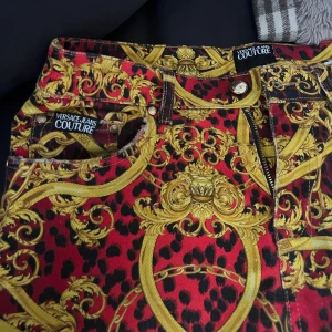 Versace Jeans Couture - Statementbyxor - Statementbyxor från Versace Jeans Couture med ikoniskt barock- och leopardmönster i rött, svart och guld. Klassiska fickor. Rak passform