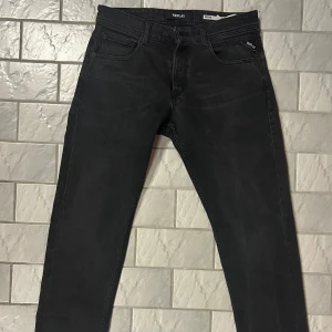 Svarta Replay jeans  - Snygga svarta jeans från Replay med klassisk femficksdesign och diskret Replay-logga på fickan. Jeansen har en slim passform och raka ben, tillverkade i mjukt denimtyg som sitter skönt. Perfekta för dig som gillar stilrena och tidlösa jeans.