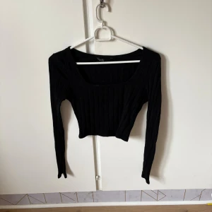 Svart ribbad croppad topp - Säljer en svart croppad topp med lång ärm och fyrkantig ringning. Toppen är ribbad och har en tight passform som framhäver siluetten. Perfekt att styla med höga jeans eller kjol för en trendig look.