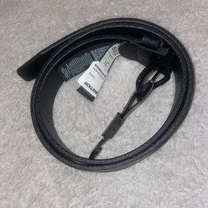 Svart skärp i skinn från Jack & Jones - Snyggt svart bälte från Jack & Jones i äkta skinn med klassiskt spänne i matt svart metall. Bältet har en stilren och enkel design med präglad logga på hällan. Perfekt accessoar för att lyfta din outfit. Namn: JACROMA LEATHER BELT NOOS. Ord pris 350kr