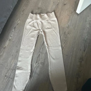 Beige ribbade leggings i storlek M - Säljer ett par beige ribbade leggings i storlek M. De har hög midja och är tillverkade i ett mjukt och stretchigt material som sitter tight och bekvämt. Perfekta för en chill och avslappnad stil.