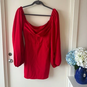 Röd kort klänning med puffärmar - Superfin röd kort klänning med långa puffärmar och draperad urringning. Klänningen har en figurnära passform och dragkedja bak.  Storlek 38, och skulle säga att den är true to size. Endast tested aldrig använd 