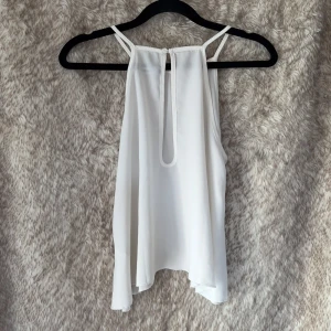Vit ärmlös linnetopp från BikBok - Säljer en stilren vit linnetopp från BikBok i storlek S. Toppen har tunna axelband, rak halsringning och en snygg öppen detalj i ryggen med knappstängning. Luftigt material.