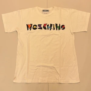Vit t-shirt från Moschino - Snygg vit t-shirt från Moschino med färgglatt tryck på framsidan. . Klassisk passform och kortärmad design. Skriv om ni har frågor