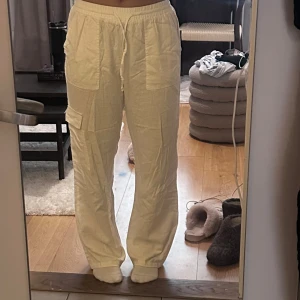 Vita linne-cargobyxor med snörning - Säljer ett par vita cargobyxor i linne med raka ben och hög midja. Byxorna har stora fickor framtill och på sidan av benen samt elastisk midja med snörning för skön passform.stil.