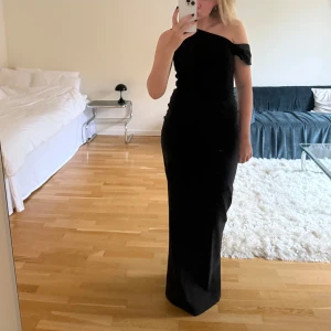Svart långklänning oneshoulder - Säljer en elegant svart långklänning med oneshoulder-design. Klänningen har en figurnära passform och är axelbandslös på ena sidan, vilket ger en stilren och modern look. Perfekt för dig som vill sticka ut med en klassisk och tidlös stil.