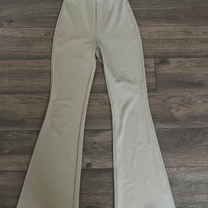 Beiga bootcut byxor med utsvängda ben - Snygga beiga byxor med riktigt utsvängda ben och bootcut-modell. De har en slät yta och är sydda i ett mjukt, stretchigt material som sitter skönt. Perfekta för dig som gillar en trendig och stilren look med lite 70-talsvibbar.
