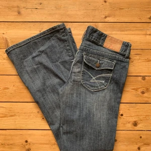 Blå bootcut jeans från Amethyst W32 L30 - Snygga blå jeans från Amethyst med bootcut passform. Jeansen har dekorativa bakfickor med lock och knapp, dubbla knappar i midjan och coola slitningar framtill. Tillverkade i bomull med en liten del polyester för extra komfort.    Storlek: W32 L30