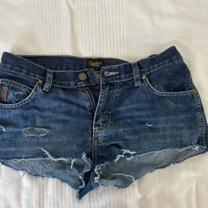 Blå jeansshorts från Crocker😍 - Snygga blå jeansshorts från Crocker med råa, fransiga kanter och slitna detaljer. Klassisk femficksmodell med dragkedja och knapp framtill. Perfekta för en avslappnad och trendig look i sommar. Pris kan diskuteras! Om du är intresserad hör av dig!!🥰