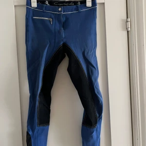 Blå ridbyxor från Copperfield, stl 160 - Snygga blå ridbyxor från Copperfield med svarta förstärkningar på insidan av benen och kontrastsömmar. Byxorna har en dragkedjeficka fram och är tillverkade i 95% bomull och 5% elastan för extra stretch och komfort.