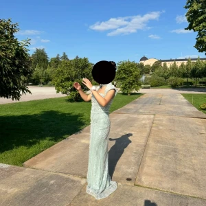 Ljusgrön långklänning med pärldetaljer - Elegant ljusgrön långklänning med glittriga pärldetaljer och hög hals. Klänningen har figurnära passform och är ärmlös, vilket ger en stilren och lyxig känsla. Perfekt för bal eller andra speciella tillfällen. De är storlek 40 i turkisk storlek men storlek 36 i svensk storlek.