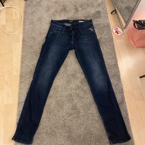 Replay Anbass slim fit jeans mörkblå - Snygga mörkblå Replay Anbass jeans i slim fit-modell. Klassisk femficksdesign, läderpatch bak och diskreta slitningar framtill. Replay-detaljer på fickorna.